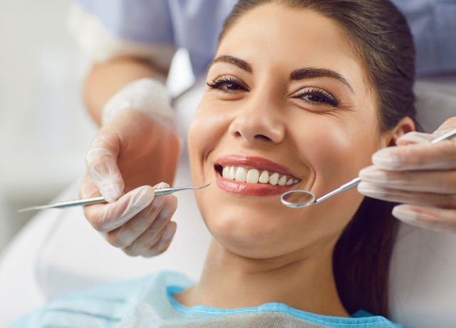 Smiling woman in dental chair receiving care, showcasing healthy teeth and clear aligner treatment in a cosmetic dentistry setting.