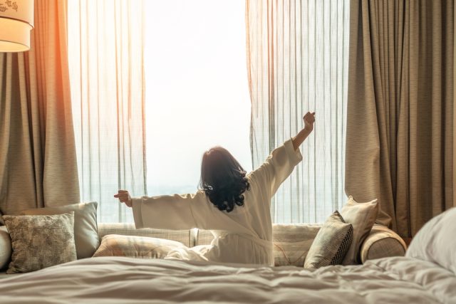 Person in a bathrobe stretching and enjoying a bright morning view from a hotel room, symbolizing relaxation during travel and the importance of dental emergency preparedness.