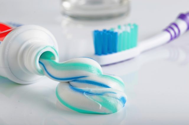 Toothpaste tube dispensing mild mint toothpaste with blue and white stripes next to a toothbrush, illustrating challenges faced by supertasters.