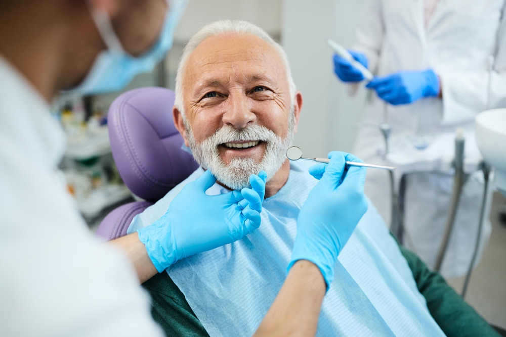 Smiling elderly man in dental chair receiving oral examination from dentist, highlighting the importance of dental care during hormonal changes and gum health.