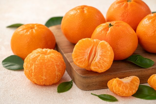 Fresh tangerines on a wooden cutting board, with one tangerine peeled and halved, emphasizing healthy fruit options for dental health.